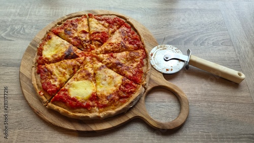 Pizza on a wooden board with a cutter resting beside it