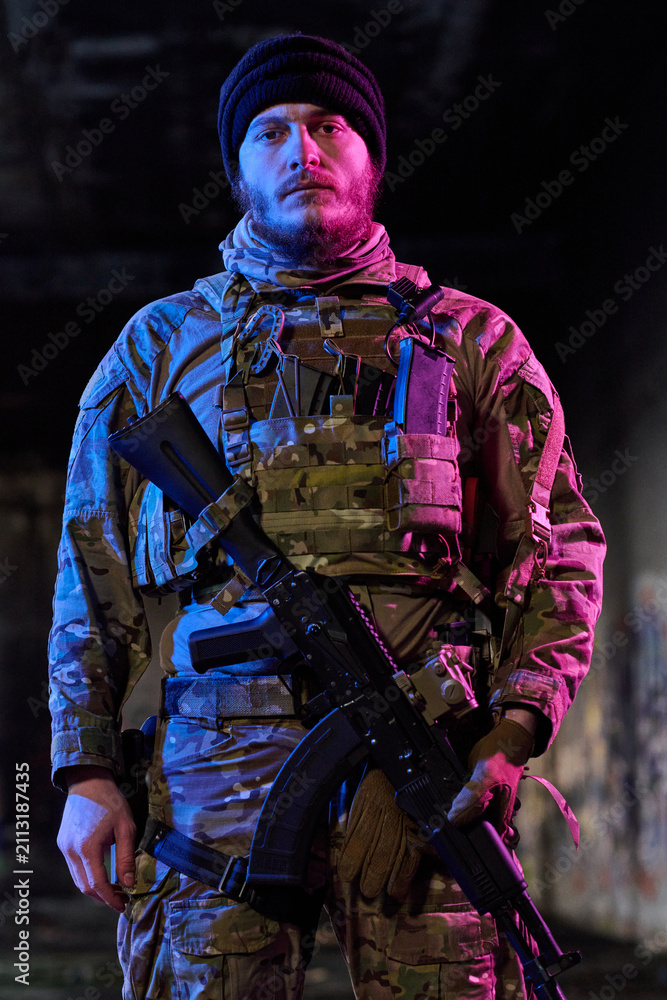 Obraz premium Armed Soldier In Camouflage Tactical Gear Holding Rifle Under Neon Urban Lighting At Night