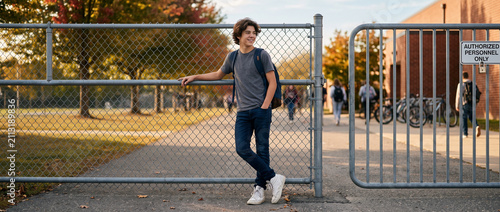 Teenage boy leaning against fence while waiting outside school  