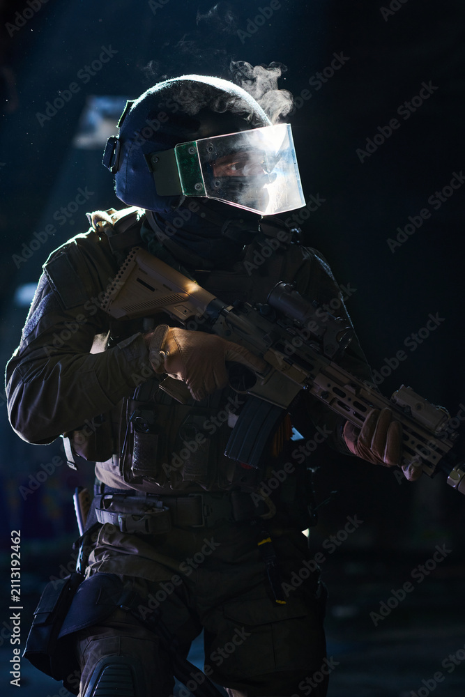 Obraz premium Armed Tactical Soldier In Riot Helmet Holding Assault Rifle During Low-Light Urban Operation