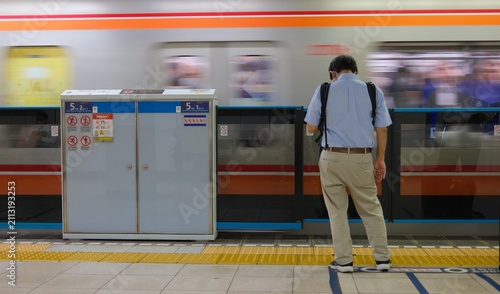 Bild auf Leinwand Back view of a Japanese commuter waiting on a subway platform with a motion blurred train passing by, Tokyo, Japan