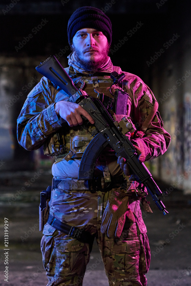 Obraz premium Armed Soldier in Camouflage Tactical Gear Holding Rifle in Urban Night Setting