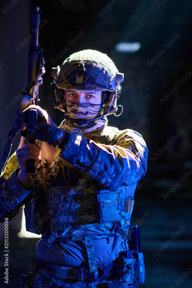 Obraz premium Armed Soldier In Tactical Gear Aiming Rifle Under Dramatic Blue Lighting In Urban Environment