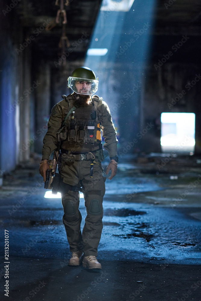 Obraz premium Armed Tactical Soldier With Protective Visor Walking Through Dimly Lit Abandoned Building