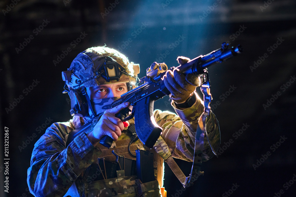 Fototapeta premium Soldier in Tactical Gear Aiming Rifle Under Dramatic Lighting During Night Training Exercise