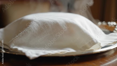 Steaming hot freshly baked bread or food covered with a white cloth on a silver tray ready to serve