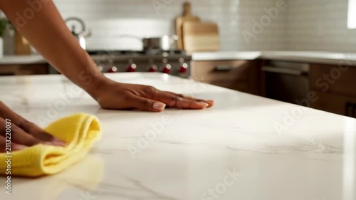 Person cleaning and wiping down a white marble kitchen countertop with a yellow microfiber cloth