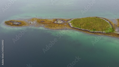 Birds fly over a small island surrounded by clear waters and green plants