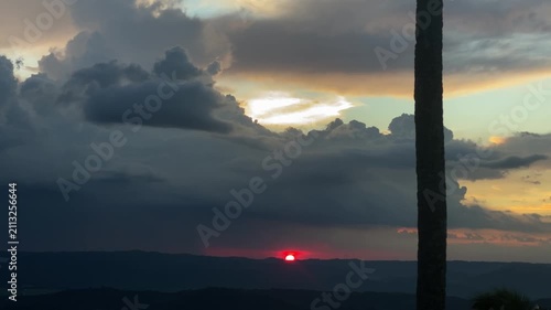 red sunset reveals a glowing horizon, with clouds scattered across the sky, catching sunlight in warm orange and yellow hues.