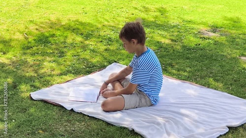 Young Boy Reading Book Sitting on Blanket in Green Park