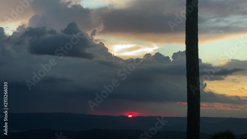Timelapse of red sunset reveals a glowing horizon, with clouds scattered across the sky, catching sunlight in warm orange and yellow hues.