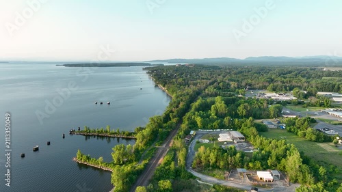 Aerial view of Lake Champlain shoreline near Plattsburgh, New York, featuring forested coastline, calm waters, and scenic mountain backdrop.