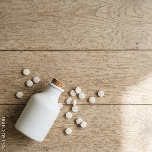 Minimalist Wellness Concept featuring White Medicine Bottle and Scattered Supplements on Natural Wood Background with Copy Space for Holistic Health Marketing