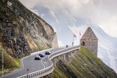 Принти на полотні Cars navigate the winding Grossglockner High Alpine Road, showcasing the engineering and scenic views of the surrounding mountainous terrain, with Austrian flags visible