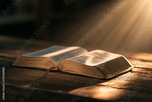 Light shines on an open bible resting on a wooden surface