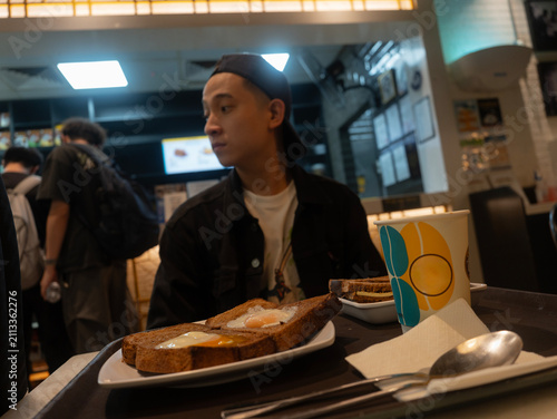 Tablou pe pânză a young man wearing a backwards cap and black jacket sits in a brightly lit cafe