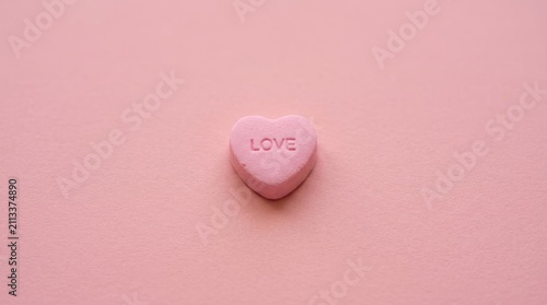 A single pink heart-shaped candy with the word 