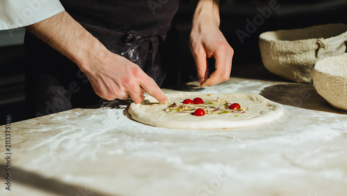 Chef preparing a delicious pizza with fresh ingredients on a floured surface.