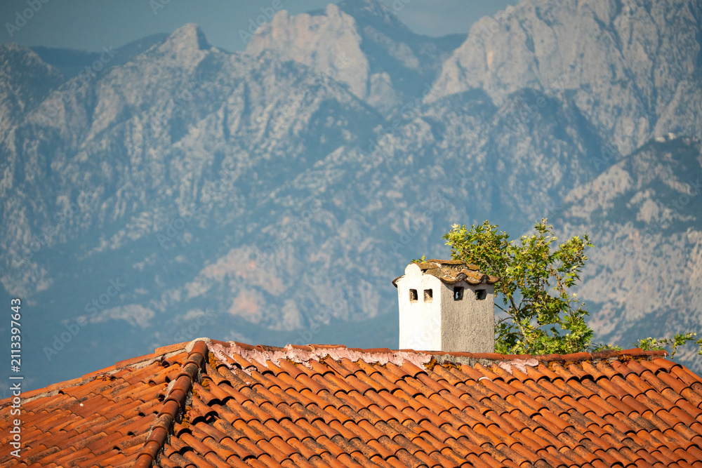 Obraz premium Traditional red tiled roof and chimney against majestic Taurus mountains in Antalya Turkey