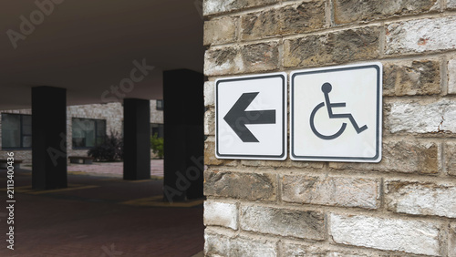 Accessible entrance direction sign with wheelchair symbol mounted on brick wall near modern residential building, highlighting inclusive design, barrier free navigation, public accessibility concept