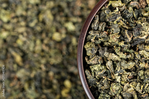 Dark wooden bowl filled with Tieguanyin on tea texture background