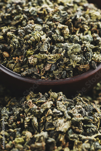 Wooden cup full of green oolong surrounded by loose tea texture