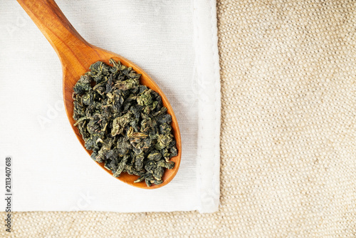 Top view closeup rustic spoon filled with loose tea on craft fabric