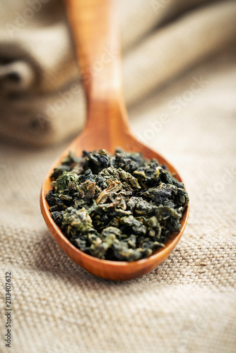 Wooden scoop of Tie Guan Yin on light burlap and linen texture