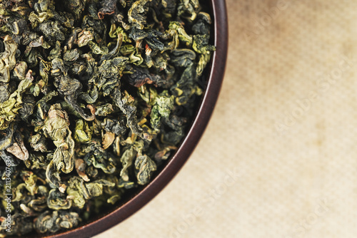 Overhead macro of green oolong in wooden cup on light burlap