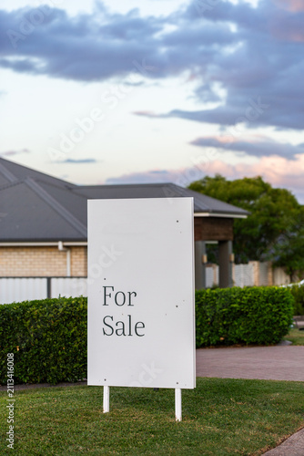 for sale sign outside home with neat green hedges