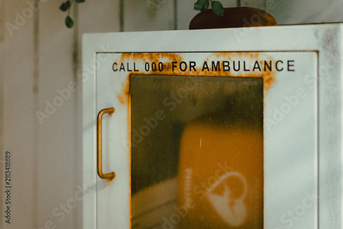 White metal cabinet mounted on a wall, labelled clearly with the text “CALL 000 FOR AMBULANCE”