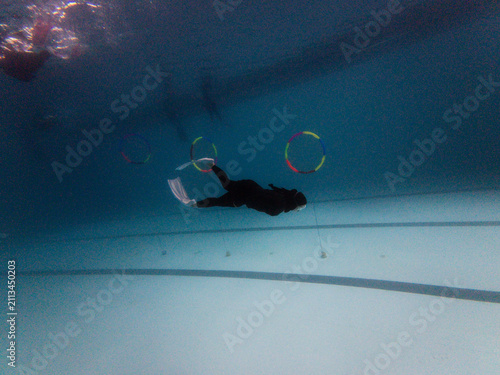 Freediver gliding horizontally underwater inside swimming pool with colorful hoops