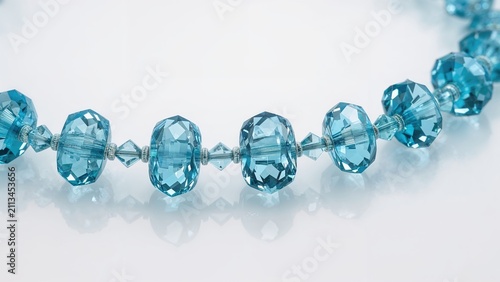 A string of blue faceted beads, possibly jewelry, arranged in a line on a white surface.