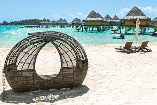 Wicker beach cabana overlooking turquoise lagoon and overwater resort villas