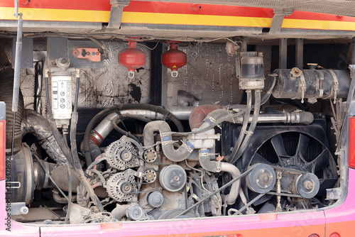 Open rear engine bay of a commercial passenger bus showing dual alternators, drive belts, fuel filter, and cooling system components.