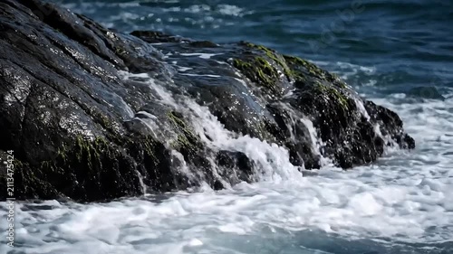 Ocean waves crash against dark volcanic rocks along the rugged coastline during a cloudy afternoon.
