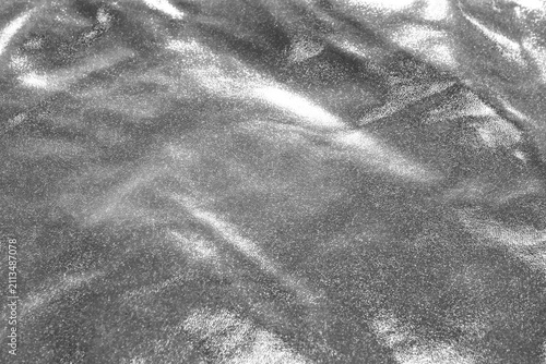Shiny silver metallic fabric texture with glittery surface and soft folds for background use
