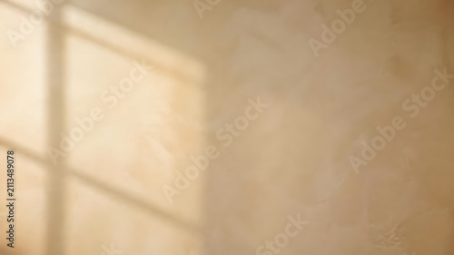 Soft natural sunlight casts a geometric window frame shadow onto a textured beige wall surface creating an elegant minimal atmosphere
