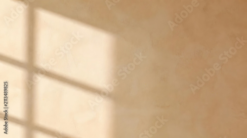 Beige textured plaster wall surface featuring soft window light shadows creating a minimalist aesthetic for modern interior design background projects