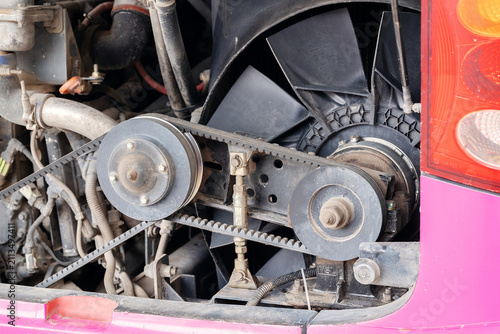 Cooling fan drive system with cogged v-belts, pulleys, tensioner, and fan blades in commercial bus engine bay.