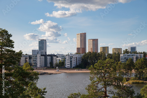 City skyline of Helsinki in Finland rising beyond a sandy beach and calm bay water.