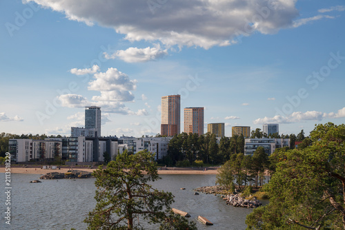 Helsinki skyline in Finland framed by pine trees along a calm bay and sandy beach.