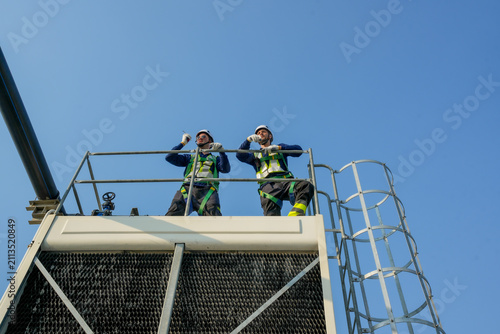 Engineer maintenance hvac cooling tower technician ladder safety rooftop industrial scene with professional climbing caged ladder for inspection and repair, focused ventilation work under clear sky