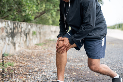 Mature man tired and leg pain during jogging at nature park. Runner has sore knees because he has been running for too long. Exercising until the injury. Training athlete work out at outdoor.