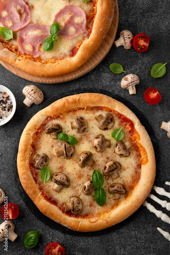 Halloween mushroom pizza with basil, cheese and spooky skeleton decoration on a dark background, creative food concept for seasonal menus. Funny food idea. Top view.