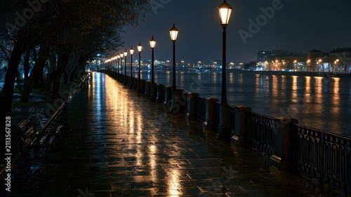 Night river promenade glowing streetlight wet pavement city waterfront urban walkway tranquil mood empty bench reflection evening calm atmosphere peaceful city river promenade with glowing
