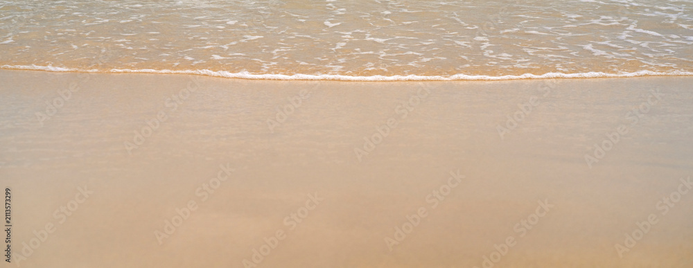 Obraz premium Clean sandy beach by the ocean, small waves with foam washing the shore, close-up view of golden yellow sand from copy space.