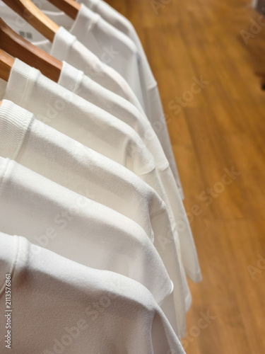 White cotton t-shirts displayed neatly on wooden hangers inside a boutique store with warm wooden flooring. Perfect for showcasing minimalist fashion, retail displays, and sustainable apparel.
