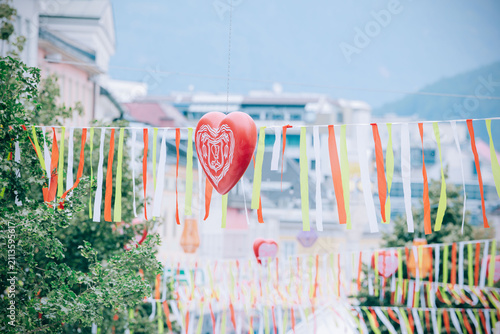 Colorful decorations with heart-shaped ornaments and vibrant ribbons hanging across a street during the Villacher Kirchtag festival in Austria