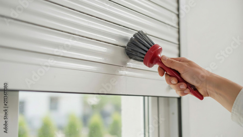 Person cleaning white window roller shutter with round duster brush